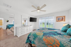 Une chambre à coucher comprenant un lit, une commode, un téléviseur et un ventilateur de plafond.