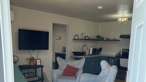 Een woonkamer met een bank, fauteuils, een televisie en een keuken op de achtergrond.