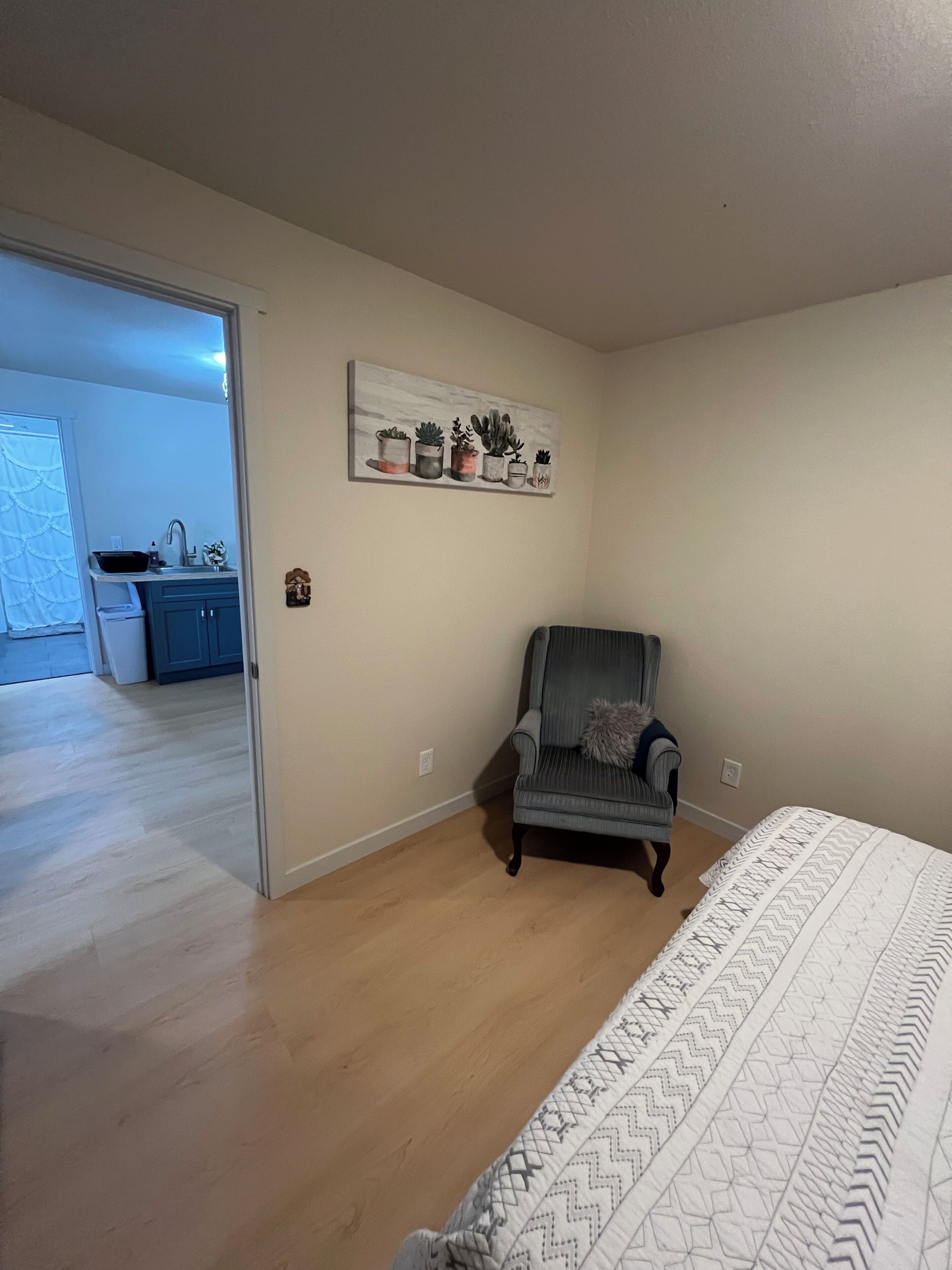 Een slaapkamer met een bed, een stoel, een kunstwerk aan de muur en uitzicht op de aangrenzende keuken.