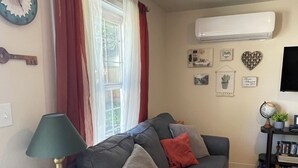 Een woonkamer met een grijze bank, een klein bijzettafeltje met een lamp, een boekenkast en een wereldbol aan de muur.