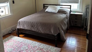A bedroom with a bed, a nightstand, a lamp, a window with blinds, and a rug. - Beautiful Family-Friendly 3BR Home in Portland North Back Cove (Portland)