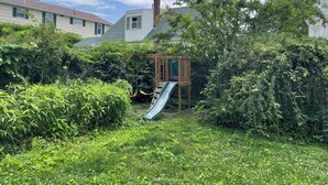 A backyard with a wooden play structure, a slide, and dense greenery. - Beautiful Family-Friendly 3BR Home in Portland North Back Cove (Portland)