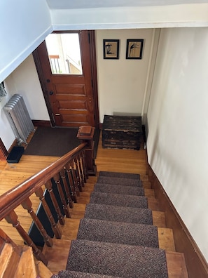 Eine Holztreppe mit Geländer, einem Heizkörper und einer Tür zu einem Außenbereich.