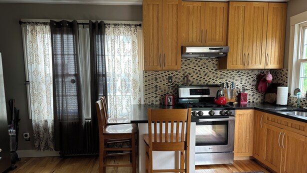 A kitchen with wooden cabinets, a gas stove, an oven, a refrigerator, and a dining table with chairs. - Beautiful Family-Friendly 3BR Home in Portland North Back Cove (Portland)