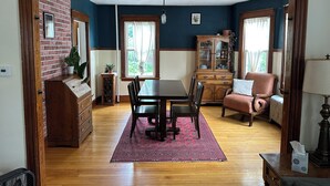 A dining area with a wooden table, chairs, a red rug, a cabinet, and a chair with a cushion. - Beautiful Family-Friendly 3BR Home in Portland North Back Cove (Portland)