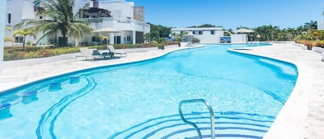 A swimming pool with clear blue water, lounge chairs, and a palm tree.