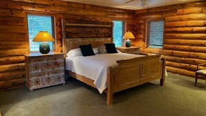 A log cabin-style bedroom with a wooden bed, two bedside tables with lamps, and a ceiling fan. - Log Cabin in Kirkland, Arizona (Kirkland)
