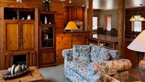 A cozy living room with a floral sofa, wooden cabinets, and a dining area with a table and chairs. - Log Cabin in Kirkland, Arizona (Kirkland)