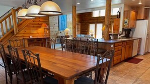 A wooden dining table with chairs, a kitchen area with wooden cabinets, and a staircase. - Log Cabin in Kirkland, Arizona (Kirkland)