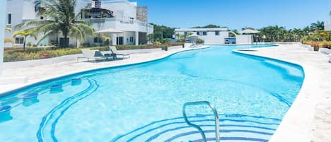 A swimming pool with clear blue water, a pool ladder, and lounge chairs.