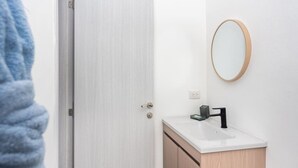 A bathroom with a white door, a wooden vanity, a black faucet, and a round mirror on the wall.