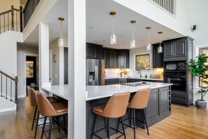 A modern kitchen with a central island, bar stools, dark cabinetry, and pendant lighting. - Modern Mtn Retreat, Views, Game Rm, Sauna, Poker (McGaheysville)