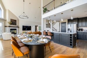 A spacious living area with a dining table set for six, a fireplace, a TV, and a kitchen with dark cabinets and stainless steel appliances. - Modern Mtn Retreat, Views, Game Rm, Sauna, Poker (McGaheysville)