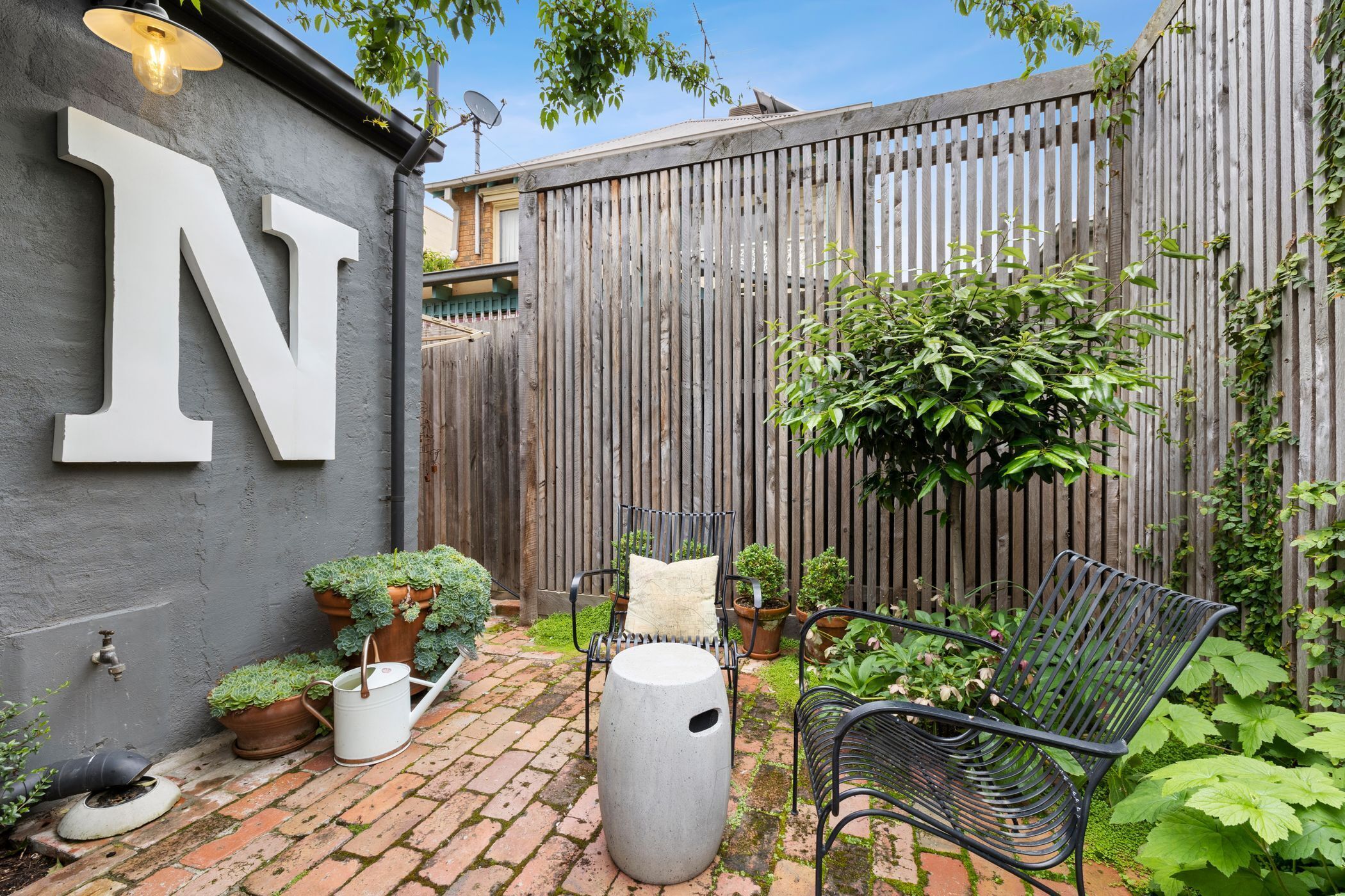A patio with a metal chair, a potted plant, and a large letter 'N' on a wall.