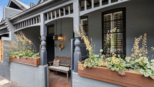 A building with a grey facade, wooden bench, and planter boxes with plants. - Your Richmond Home: Calm, Character, Walkable (Richmond)
