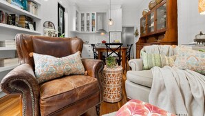 A living room with a brown leather armchair, a round side table with a plant, a white sofa, and a wooden cabinet with baskets. - Your Richmond Home: Calm, Character, Walkable (Richmond)