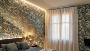 A bedroom with a bed, a nightstand, a lamp, and a window with curtains. - Welcome to our vacation home, "Azzurro Garda🩵," in Sirmione! (Sirmione)
