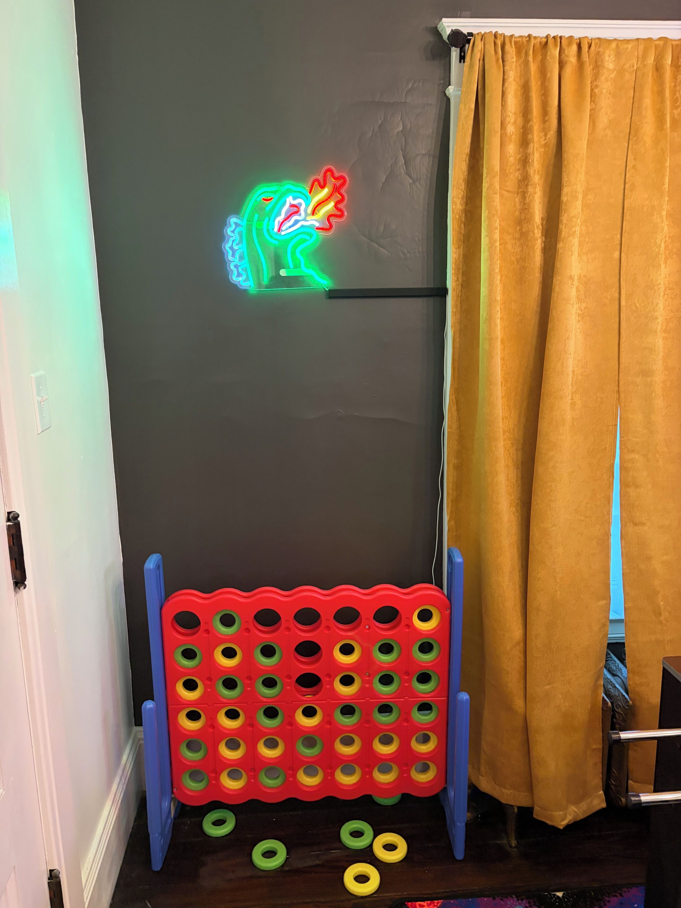 Een kamer met neonverlichting, een speelbord en een geel gordijn.