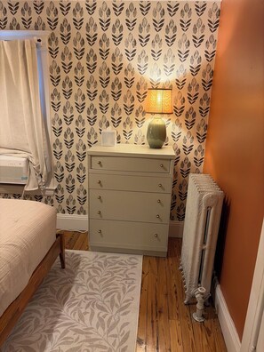 A bedroom with a bed, dresser, radiator, and patterned wallpaper. - Fun Eclectic Designer Home in Historic Strathmore (Syracuse)