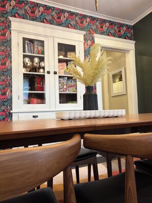 Un comedor con una mesa de madera, sillas, un aparador con adornos y un papel tapiz floral.