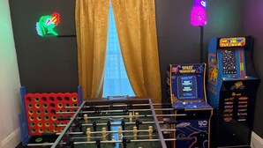 Een kamer met een tafelvoetbaltafel, twee gokautomaten en een raam met gordijnen.