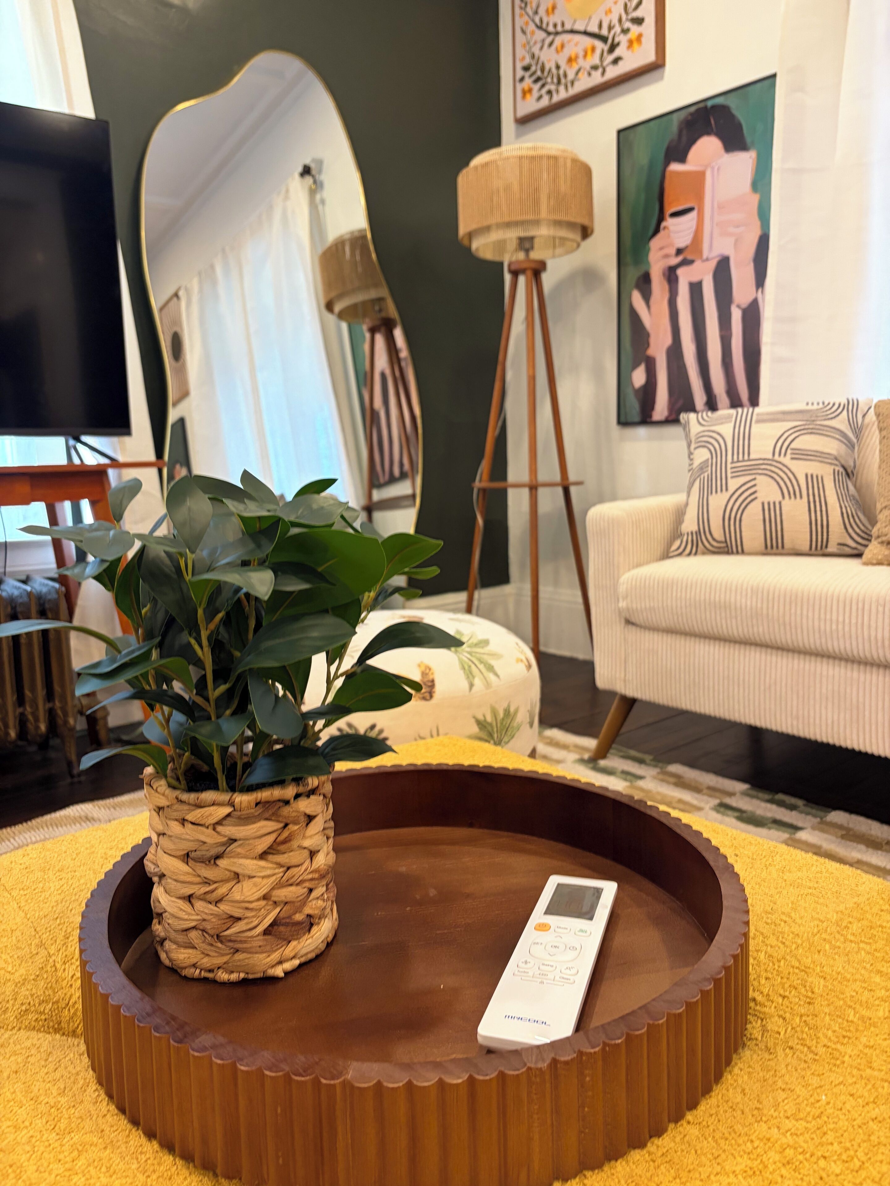 A round wooden tray with a woven plant holder and a remote control on a yellow rug.