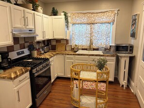 Una cocina con gabinetes blancos, estufa, microondas y una silla de mimbre.