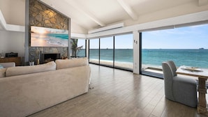 Een ruime woonkamer met een groot raam met uitzicht op zee, een stenen muur en een open haard.