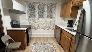 A compact kitchen with a refrigerator, stove, and a coffee maker. - Room - 202 - King Bed (Syracuse)