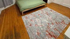 A room with a bed, a rug, wooden flooring, a door, and a picture on the wall. - Room - 202 - King Bed (Syracuse)