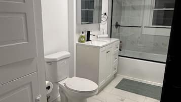 A bathroom with a toilet, sink, mirror, and shower area.