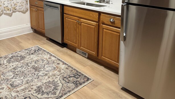 A kitchen with wooden cabinets, a stainless steel refrigerator, a coffee maker, and a patterned rug. - Room - 202 - King Bed (Syracuse)