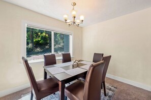 Un comedor con una mesa y sillas, una araña y un ventanal con vistas a follaje.