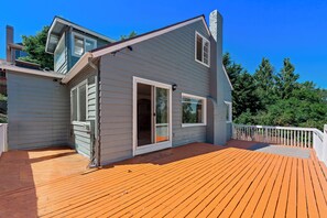 Ein zweistöckiges Haus mit einer Holzdachterrasse und einer großen Schiebeglastür.
