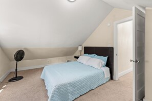 A bedroom with a bed, a standing fan, a nightstand, and a door. - Private 4BR • Free Parking • Near Airport & Seattle (Tukwila)