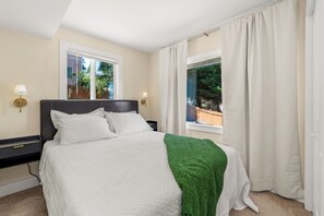 Ein Hotelzimmer mit einem Bett, zwei Nachttischen, einem Fenster mit Vorhängen und Blick ins Freie.