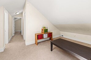 Um quarto com teto inclinado, um banco de madeira, uma mesa pequena e um móvel para guardar brinquedos.