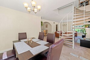 Ein Essbereich mit einem Tisch für vier Personen, einer Chandelierleuchtre und einer Treppe zu einer oberen Ebene.