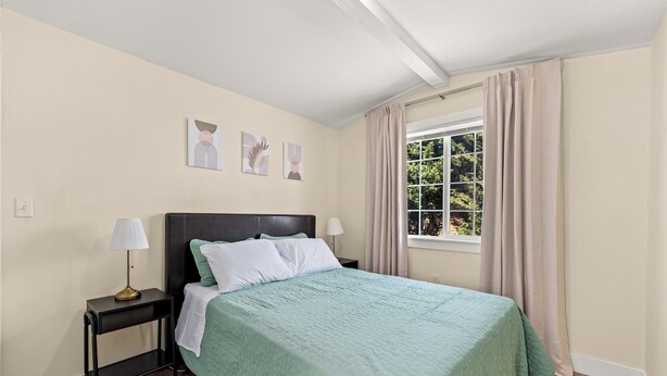 Ein Schlafzimmer mit einem Bett, Nachttischen, einem Fenster mit Vorhängen und Wandbildern.