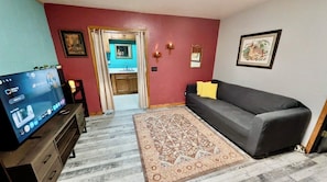 A living room with a television, a sofa, a patterned rug, and a door leading to a bathroom. - One King bedroom Boho Retreat 2.6 miles from
Downtown (Eureka Springs)