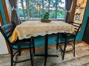 A dining table with a lace tablecloth, surrounded by chairs, set against a window with a view of trees. - One King bedroom Boho Retreat 2.6 miles from
Downtown (Eureka Springs)