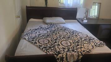 A neatly made bed with a patterned bedspread, a bedside table with a lamp, and a wall-mounted mirror.