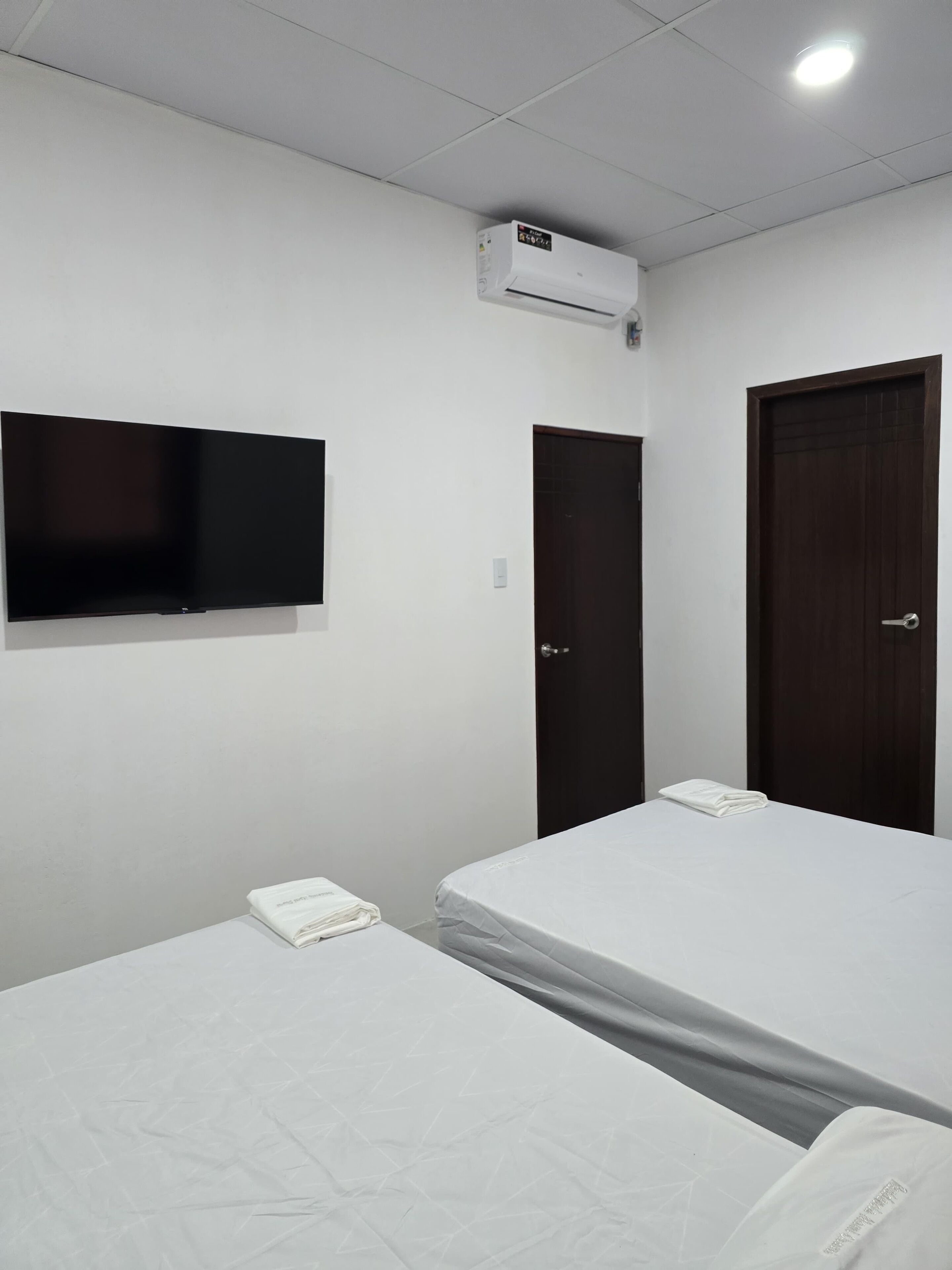 A room with two beds, a flat-screen TV mounted on the wall, a door, and an air conditioning unit.