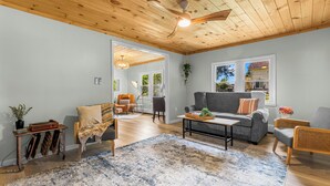 A spacious living room with a wooden ceiling, a grey sofa, a coffee table, and a blue patterned rug.