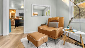 A modern living room with a leather sofa, a matching ottoman, a side table with books, a floor lamp, and a large mirror on the wall.