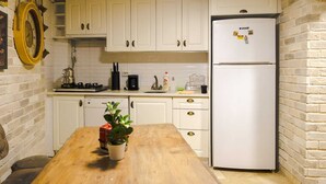 Una cocina con armarios blancos, un refrigerador blanco, una mesa de madera y una planta en maceta.