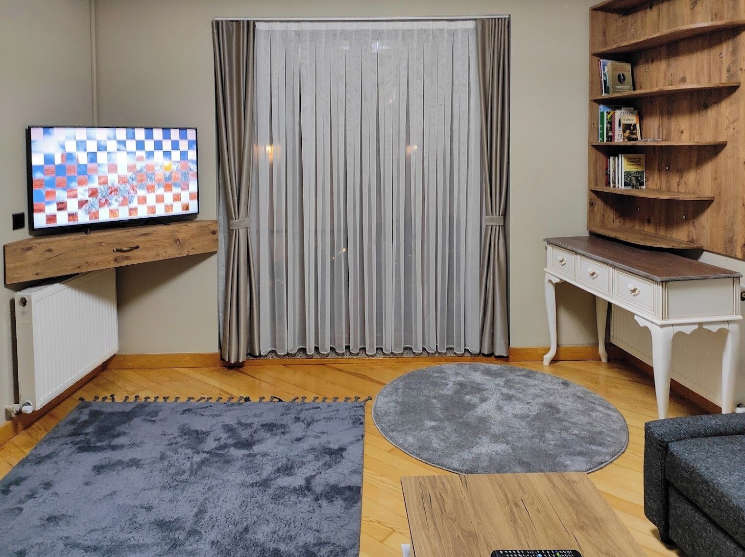 A living room with a television, a wooden bookshelf, a white side table, and a grey rug.