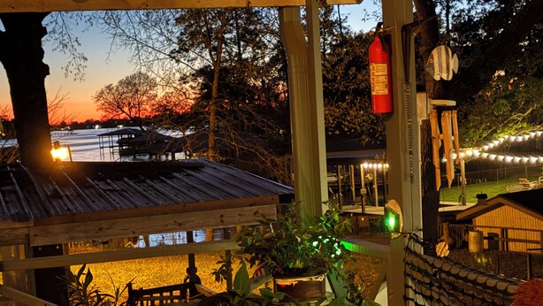 Una terraza de madera con plantas en macetas, un extintor y luces colgantes.