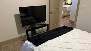 A bed with white bedding, a black blanket, and a TV on a stand. - Cozy 1-bedroom apartment with AC in peaceful Houston (Houston)