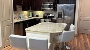 A kitchen with dark wood cabinets, stainless steel appliances, a granite countertop, and white bar stools. - Cozy 1-bedroom apartment with AC in peaceful Houston (Houston)